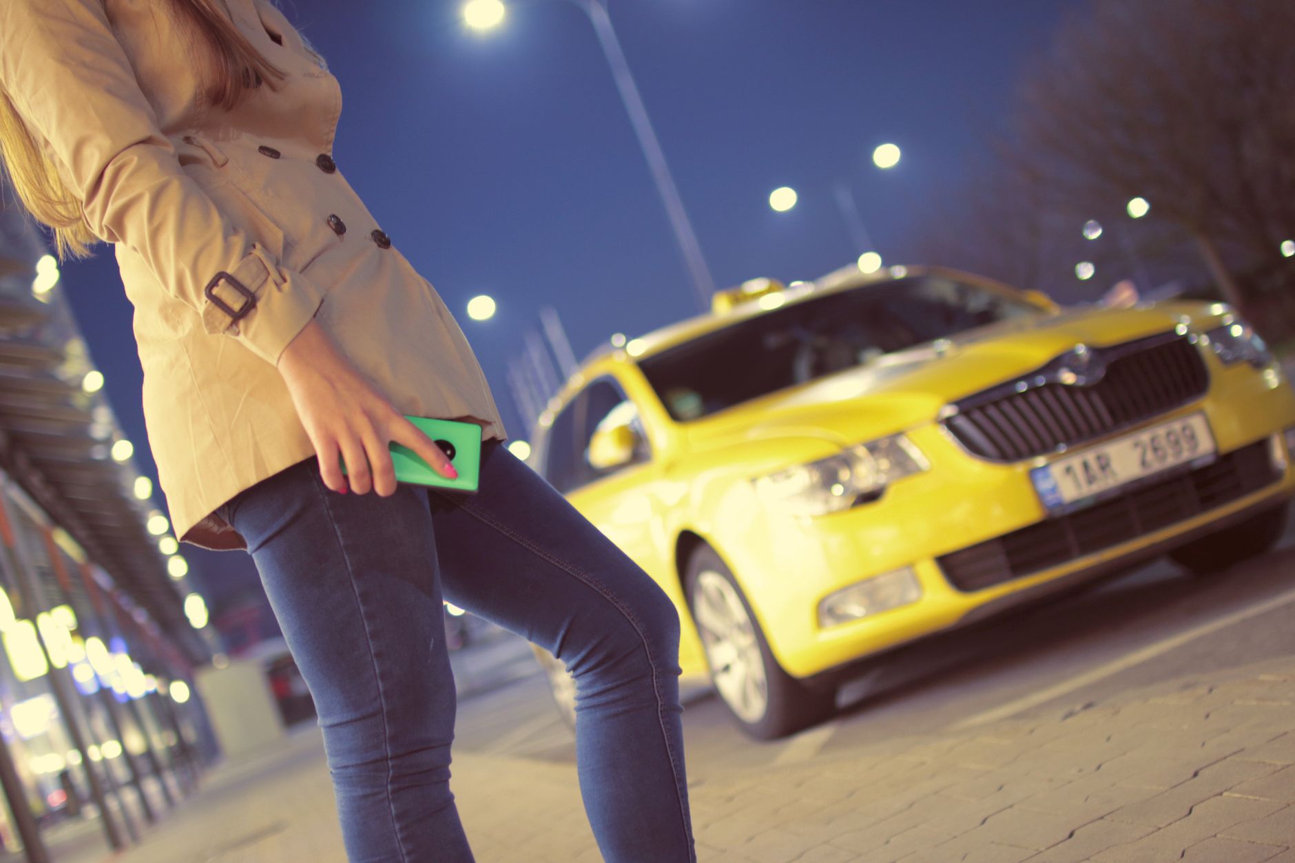 Jak bezpiecznie zamówić taxi w nocy w dużym mieście – praktyczny poradnik dla pasażerów Kobieta z telefonem przy żółtej taksówce nocą w oświetlonym mieście