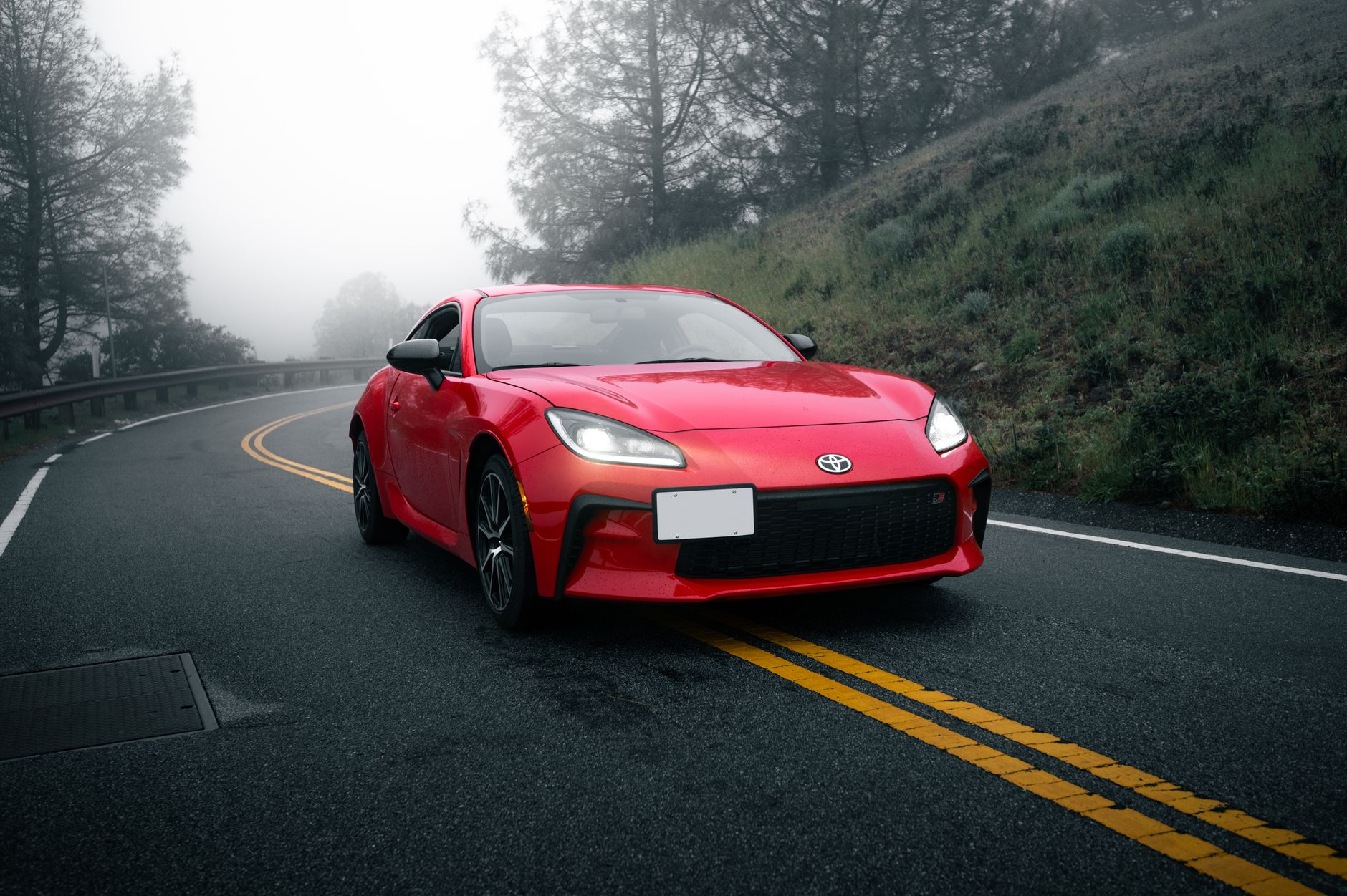 Czerwona sportowa Mazda jedzie krętą drogą we mgle