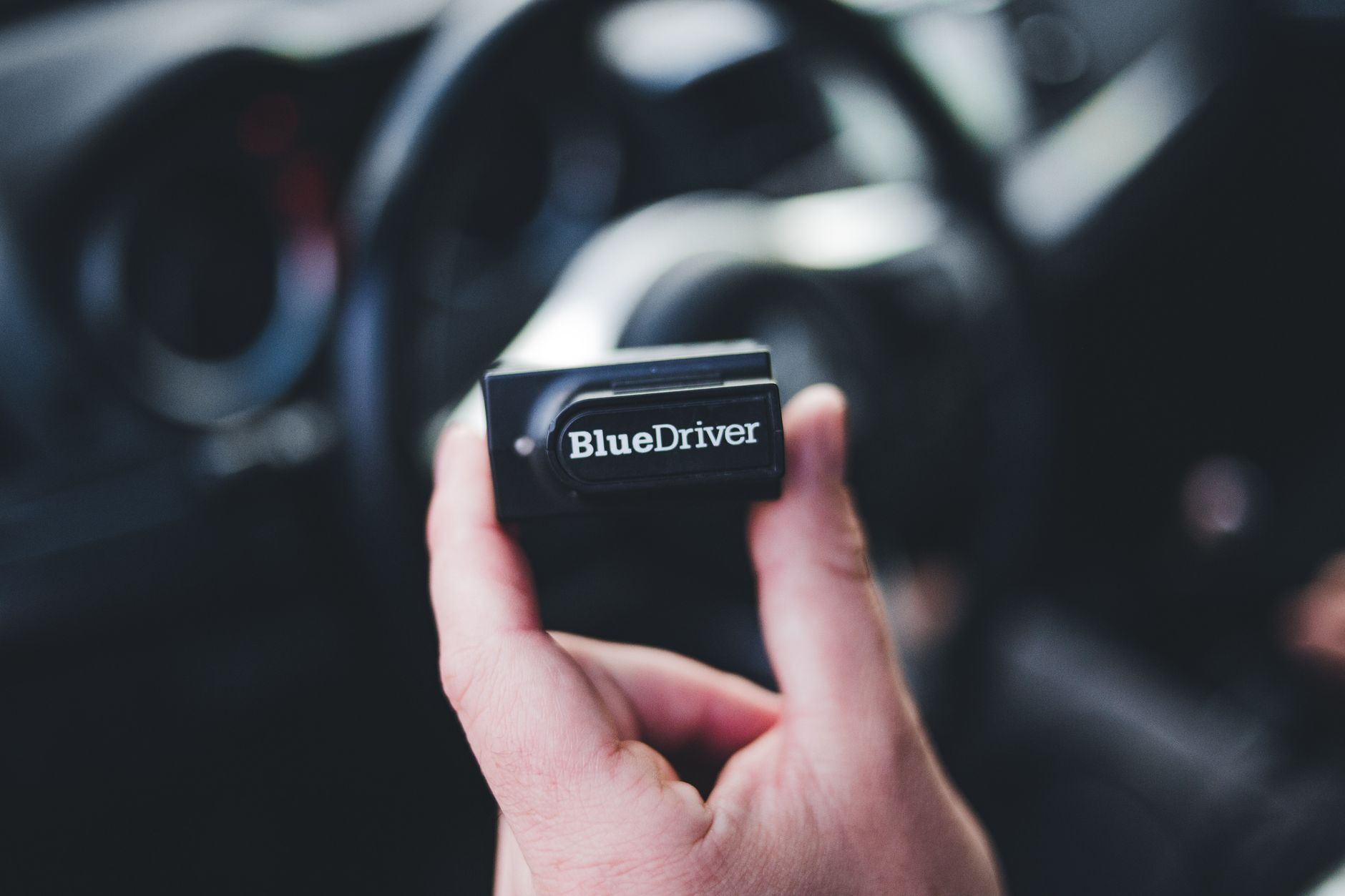 Dłoń trzymająca skaner OBD2 Bluedriver wewnątrz auta Mazda