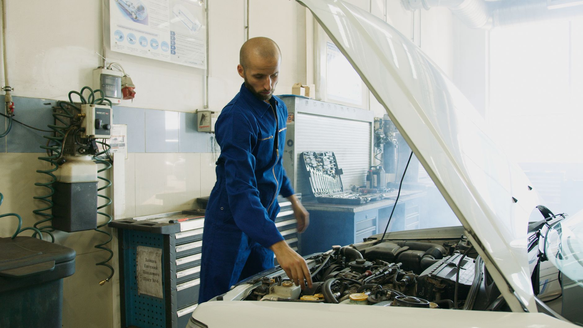 Mechanik w niebieskim uniformie sprawdza silnik używanego Maserati w warsztacie